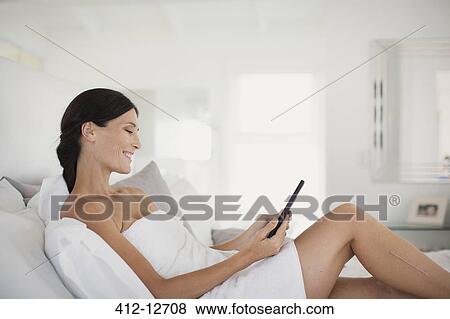 Stock Photo - Woman in towel using digital tablet on bed. Fotosearch