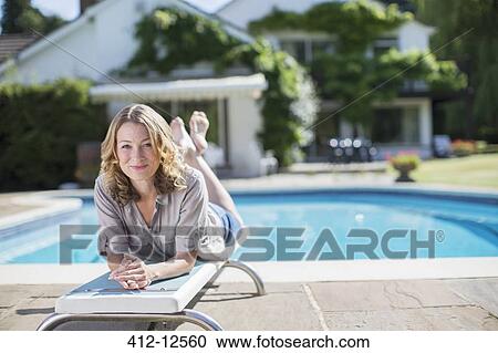 Stock Image - Woman laying on diving board at poolside. Fotosearch