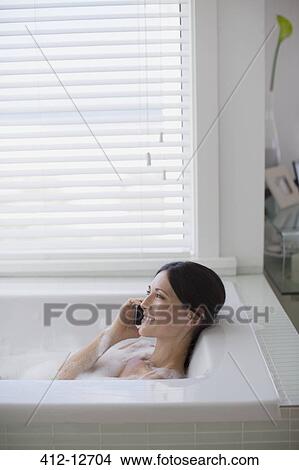 Picture - Woman talking on cell phone in bathtub. Fotosearch