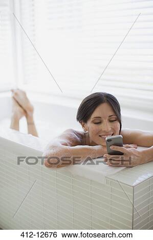 Stock Photograph - Woman using cell phone in bathtub. Fotosearch