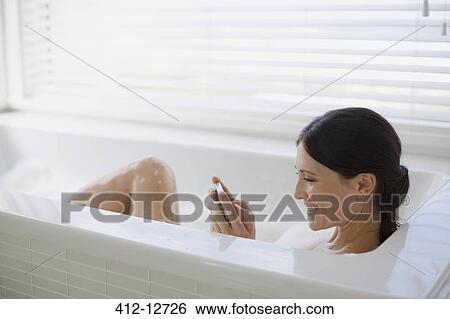 Stock Photograph - Woman using cell phone in bubble bath. Fotosearch