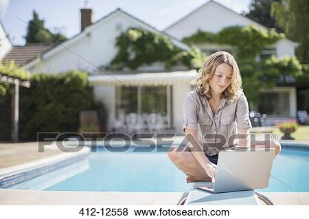 Stock Photo - Woman using laptop on diving board at poolside. Fotosearch
