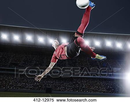 Stock Photography - Soccer player kicking ball in mid-air on field. Fotosearch