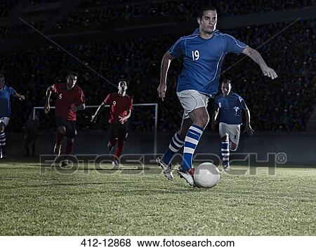 Soccer players chasing ball on field View Large Photo Image Stock Photo - Soccer players chasing ball on field. Fotosearch