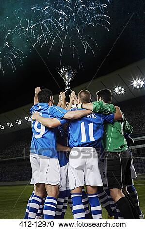 Stock Image - Soccer team cheering with trophy on field. Fotosearch