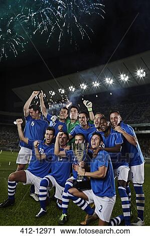 Stock Image - Soccer team cheering with trophy on field. Fotosearch