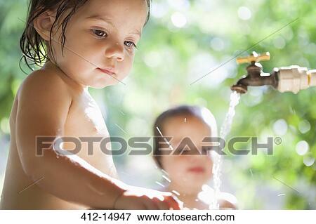 Stock Photo - Baby girls playing in water spout outdoors. Fotosearch