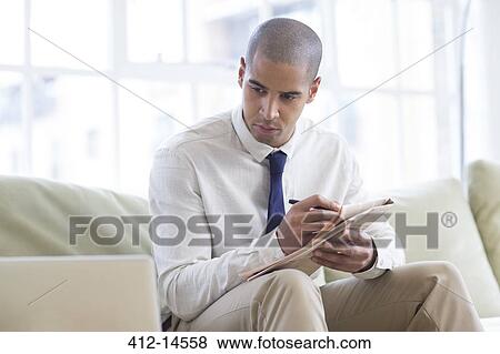 Stock Photo - Businessman making notes from laptop on sofa. Fotosearch
