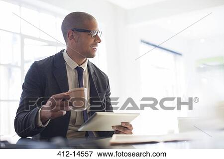 Stock Photo - Businessman using digital tablet and drinking coffee. Fotosearch