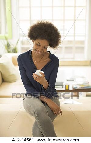 Stock Image - Businesswoman using cell phone on sofa. Fotosearch