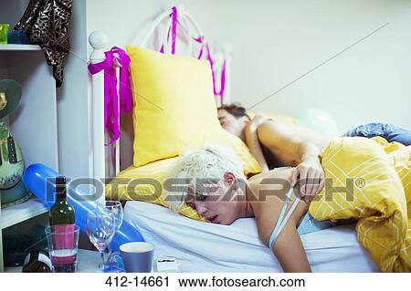 Stock Image - Couple sleeping in bed the morning after a party. Fotosearch