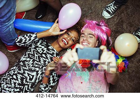 Picture - Couple taking self-portrait with cell phone on floor at party. Fotosearch