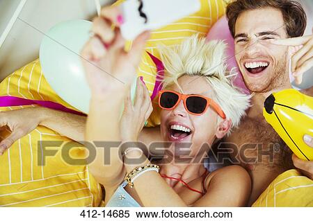 Couple taking self-portraits in bed at party View Large Photo Image Stock Photography - Couple taking self-portraits in bed at party. Fotosearch