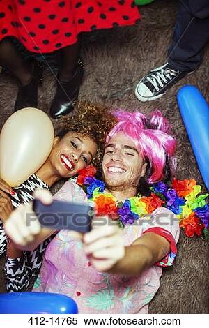 Stock Photography - Couple taking self-portraits with camera phone on floor at party. Fotosearch