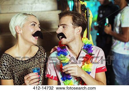 Stock Image - Couple wearing fake mustaches at party. Fotosearch