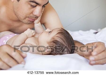 Stock Photography - Father admiring baby girl on bed. Fotosearch