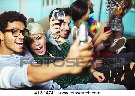 Stock Image - Friends drinking on sofa at party. Fotosearch