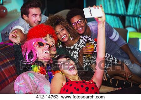 Stock Image - Friends taking pictures on sofa at party. Fotosearch