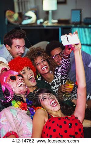 Friends taking self-portrait with camera phone on sofa at party View Large Photo Image Stock Image - Friends taking self-portrait with camera phone on sofa at party. Fotosearch