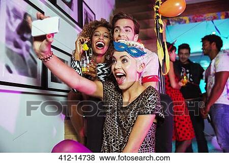 Friends taking self-portraits with camera phone at party View Large Photo Image Stock Photo - Friends taking self-portraits with camera phone at party. Fotosearch