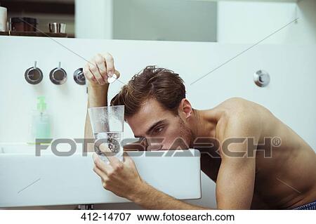 Stock Photo - Hungover man watching effervescent tablets in bathroom. Fotosearch