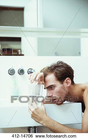 Stock Photograph - Hungover man watching effervescent tablets in bathroom. Fotosearch