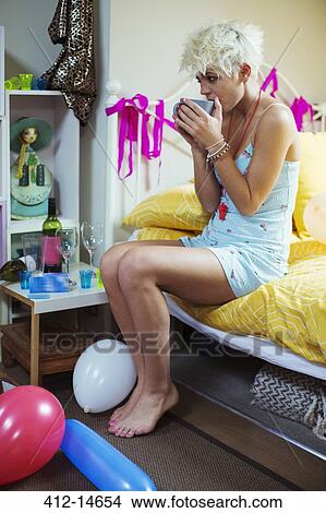 Picture - Hungover woman drinking cup of coffee in bed. Fotosearch