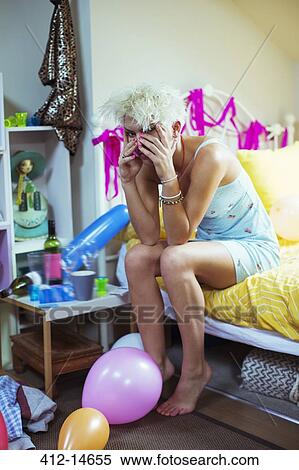 Stock Photography - Hungover woman rubbing face on bed the morning after a party. Fotosearch
