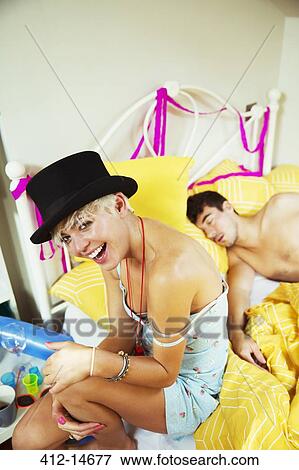 Stock Photo - Laughing woman sitting on bed the morning after a party. Fotosearch