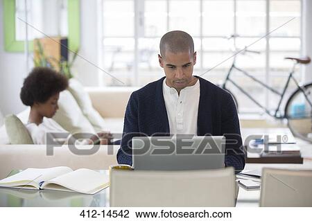 Man using laptop at desk in living room View Large Photo Image Stock Image - Man using laptop at desk in living room. Fotosearch