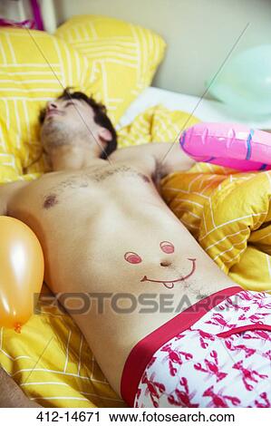 Stock Image - Man with smiley face drawing on belly sleeping after party. Fotosearch