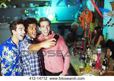 Stock Image - Men taking self-portraits with camera phone at party. Fotosearch