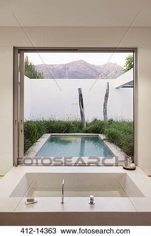 Stock Image - Modern bathroom overlooking swimming pool and mountains. Fotosearch