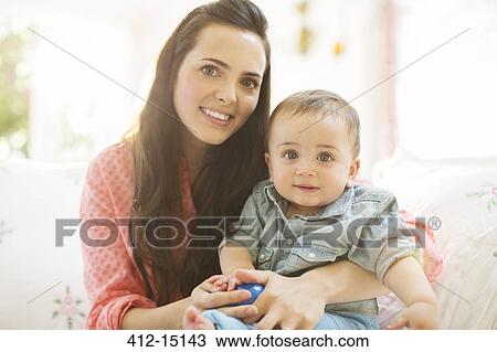 Stock Image - Mother holding baby boy on sofa. Fotosearch