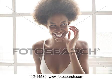 Stock Photo - Smiling woman in bra standing by window. Fotosearch