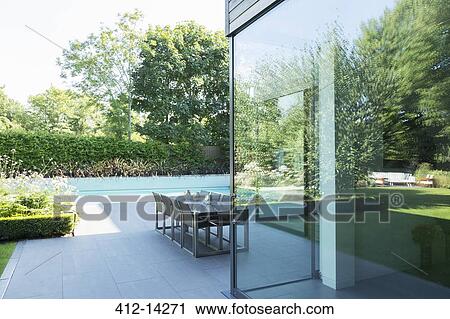 Stock Image - Table and chairs on patio by swimming pool. Fotosearch