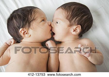 Stock Image - Twin baby girls kissing on bed. Fotosearch