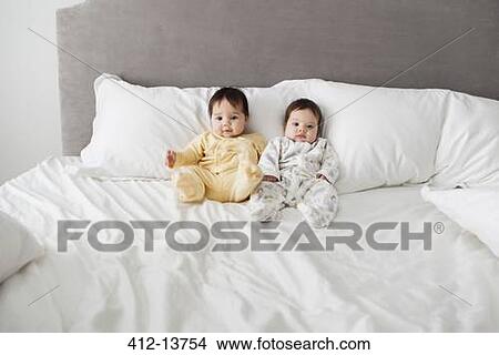 Picture - Twin baby girls sitting on bed. Fotosearch
