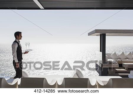 Stock Photography - Waiter serving champagne at cabana overlooking ocean. Fotosearch