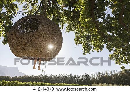 Stock Photo - Woman dangling feet from nest tree house. Fotosearch