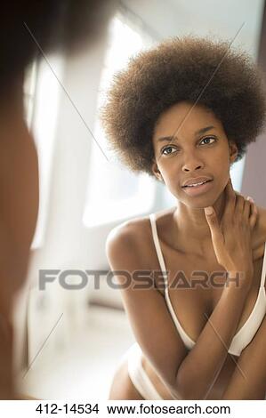 Picture - Woman in bra and panties examining herself in mirror. Fotosearch