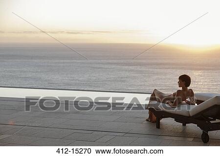 Woman in dress laying on lounge chair on patio overlooking ocean at sunset View Large Photo Image Stock Image - Woman in dress laying on lounge chair on patio overlooking ocean at sunset. Fotosearch