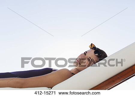 Stock Image - Woman laying on lounge chair outdoors. Fotosearch