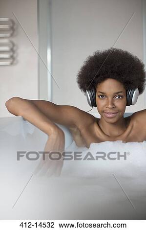 Stock Image - Woman listening to headphones in bath. Fotosearch