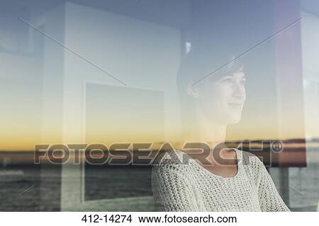 Picture - Woman overlooking sunset and ocean from window. Fotosearch