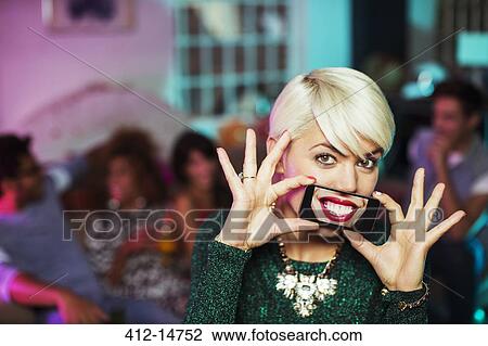 Stock Image - Woman playing with cell phone in living room at party. Fotosearch