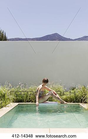 Stock Photo - Woman sitting at the edge of luxury swimming pool. Fotosearch