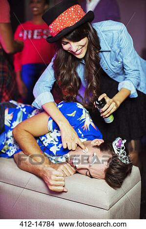 Woman spraying shaving cream on sleeping man's face at party View Large Photo Image Picture - Woman spraying shaving cream on sleeping man's face at party. Fotosearch
