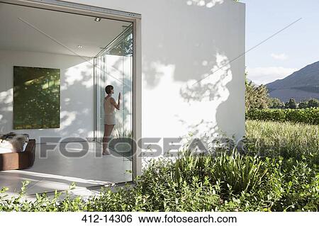 Stock Photograph - Woman standing at window in modern house. Fotosearch