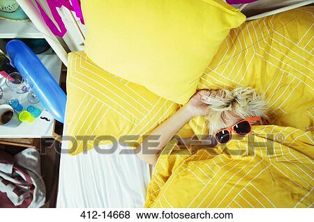 Stock Photo - Woman wearing sunglasses in bed after party. Fotosearch